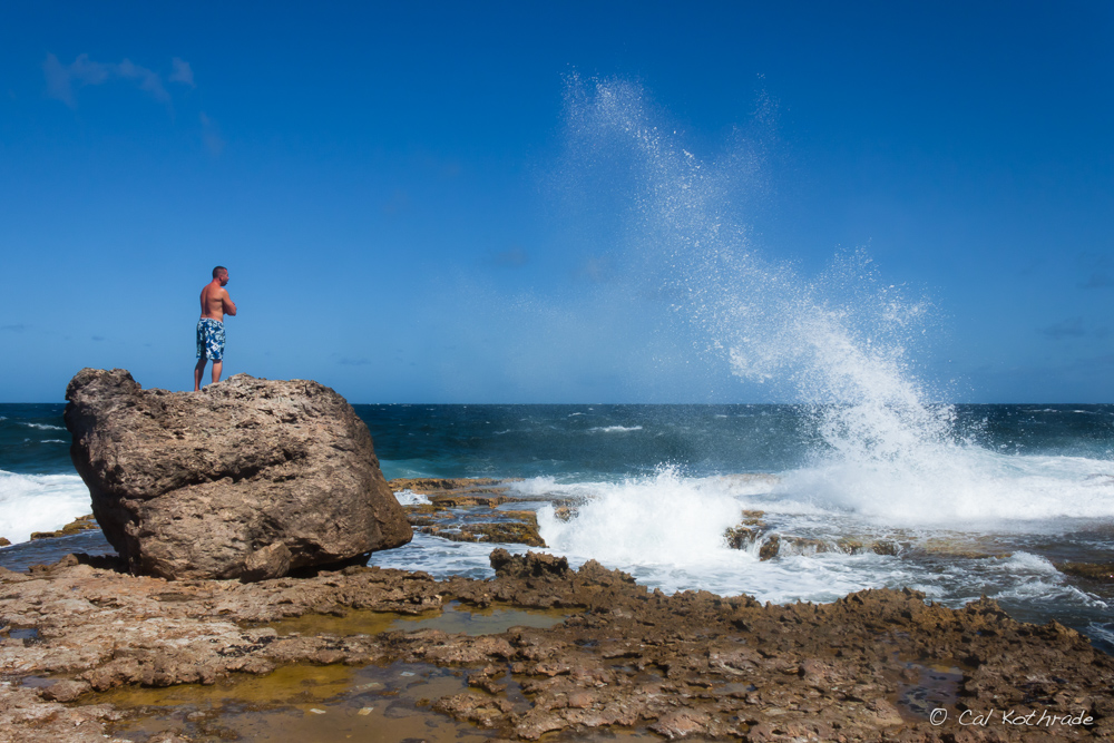 Man watches surf spray hit rocks on windward side of Bonaire.